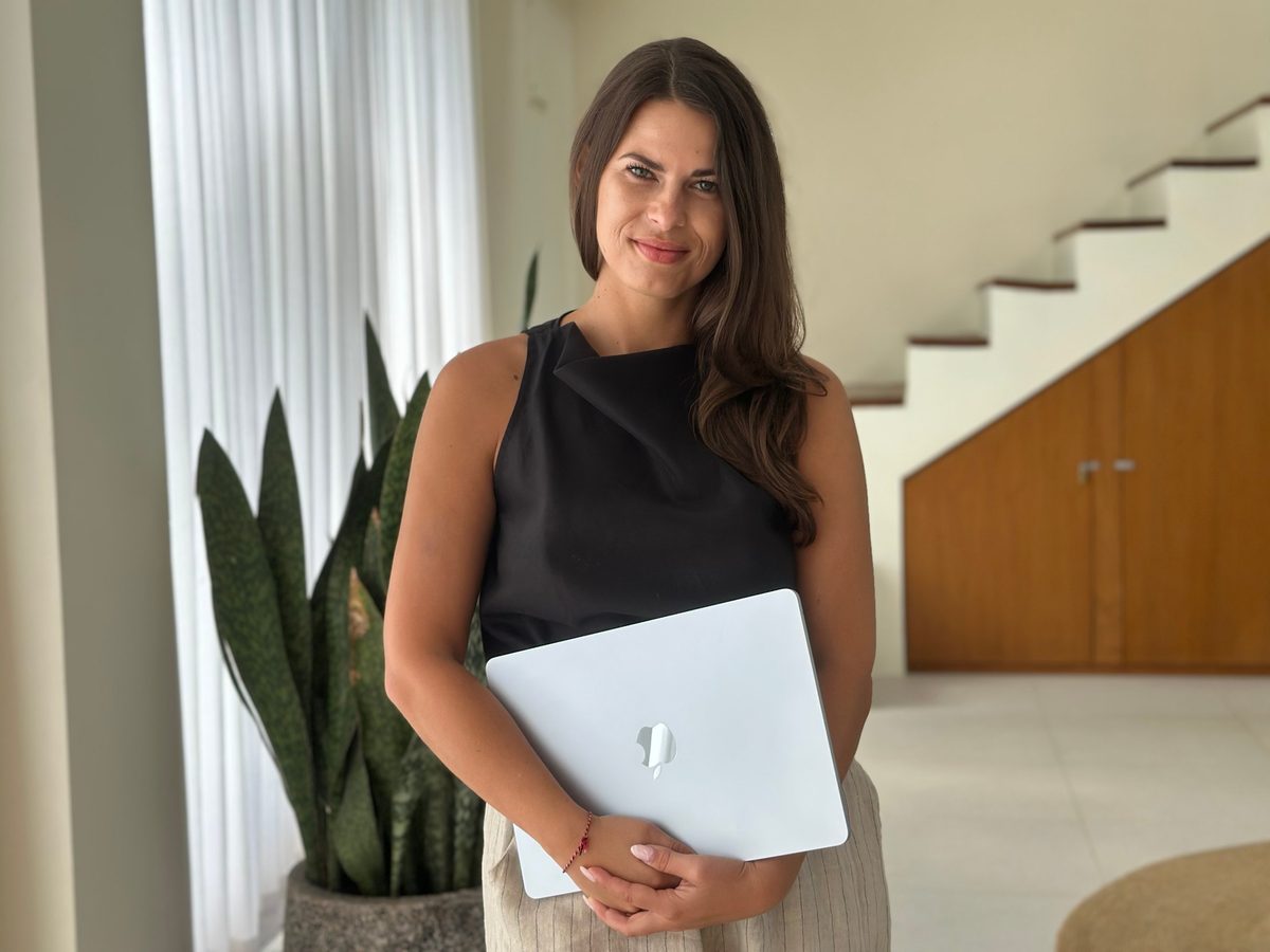 Aline Wendt standing in a bright room, holding a laptop